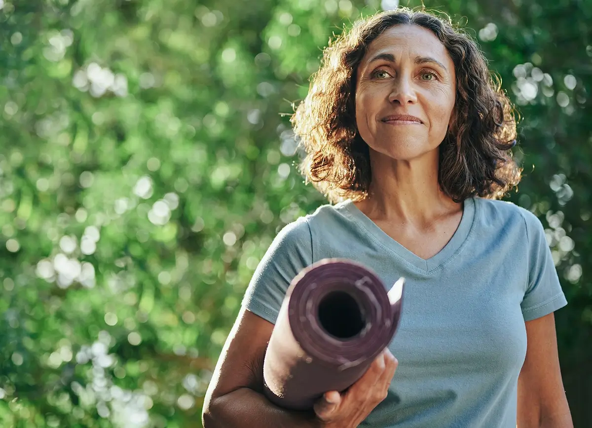 A woman holding her yoga mat and looking in the distance
