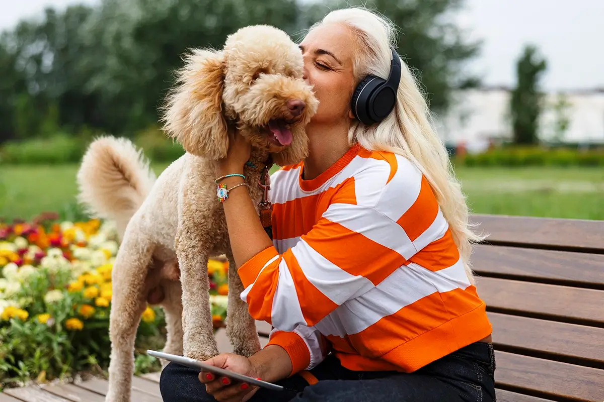 A woman interacting with her dog on a bench with her phone