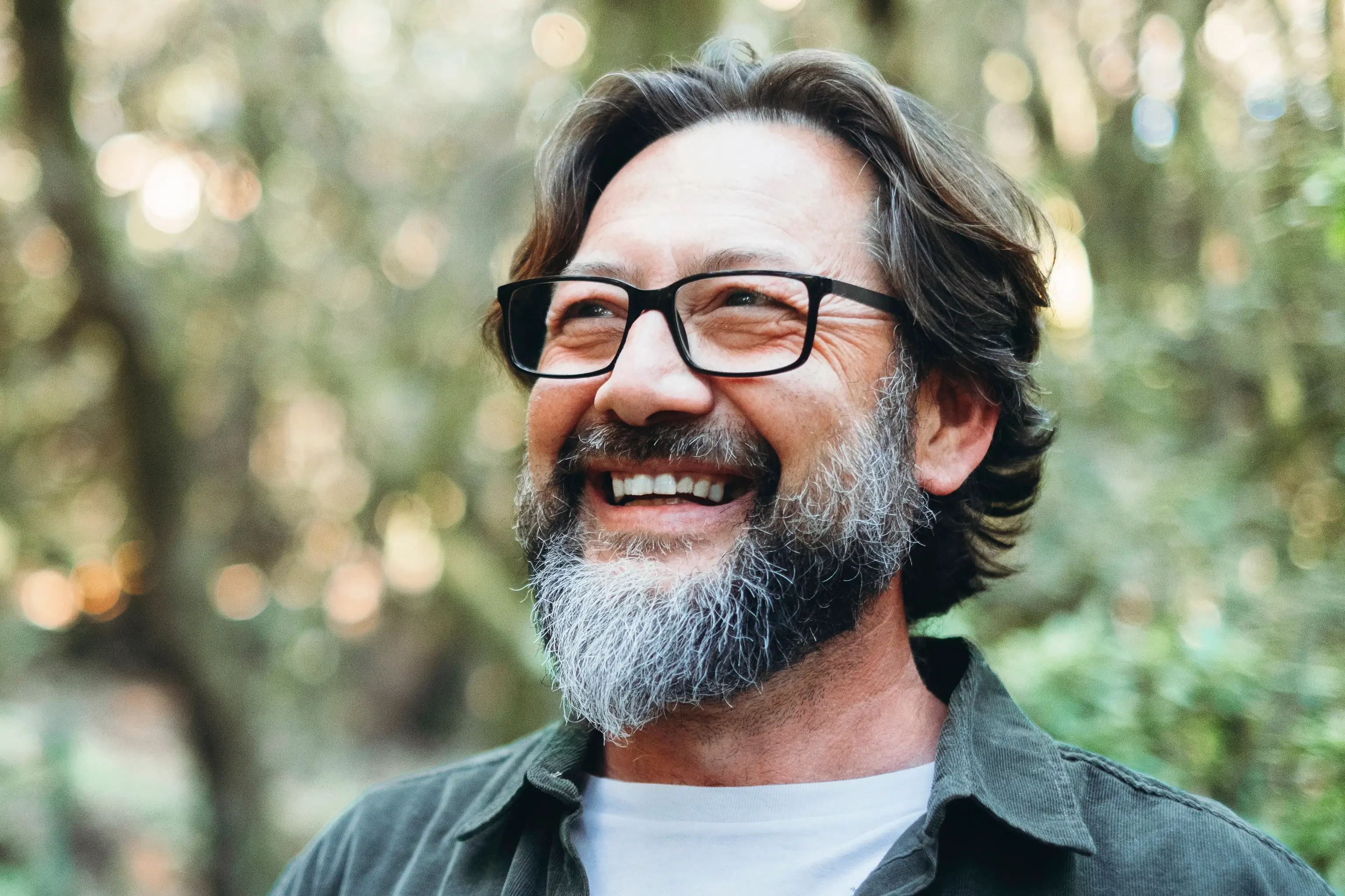 A man smiling looking out to the distance in a park like setting